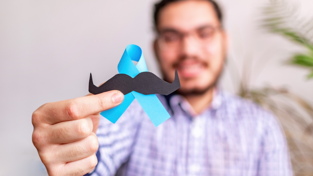 Image of an out of focus man in the background holding a blue ribbon with moustache in focus