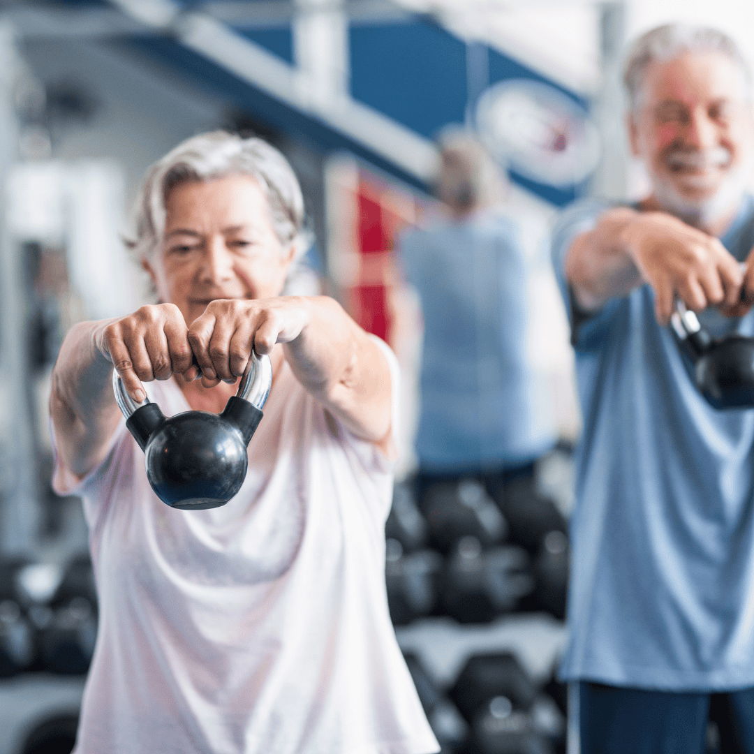 A senior couple, each lifting a kettlebell during a workout in a gym